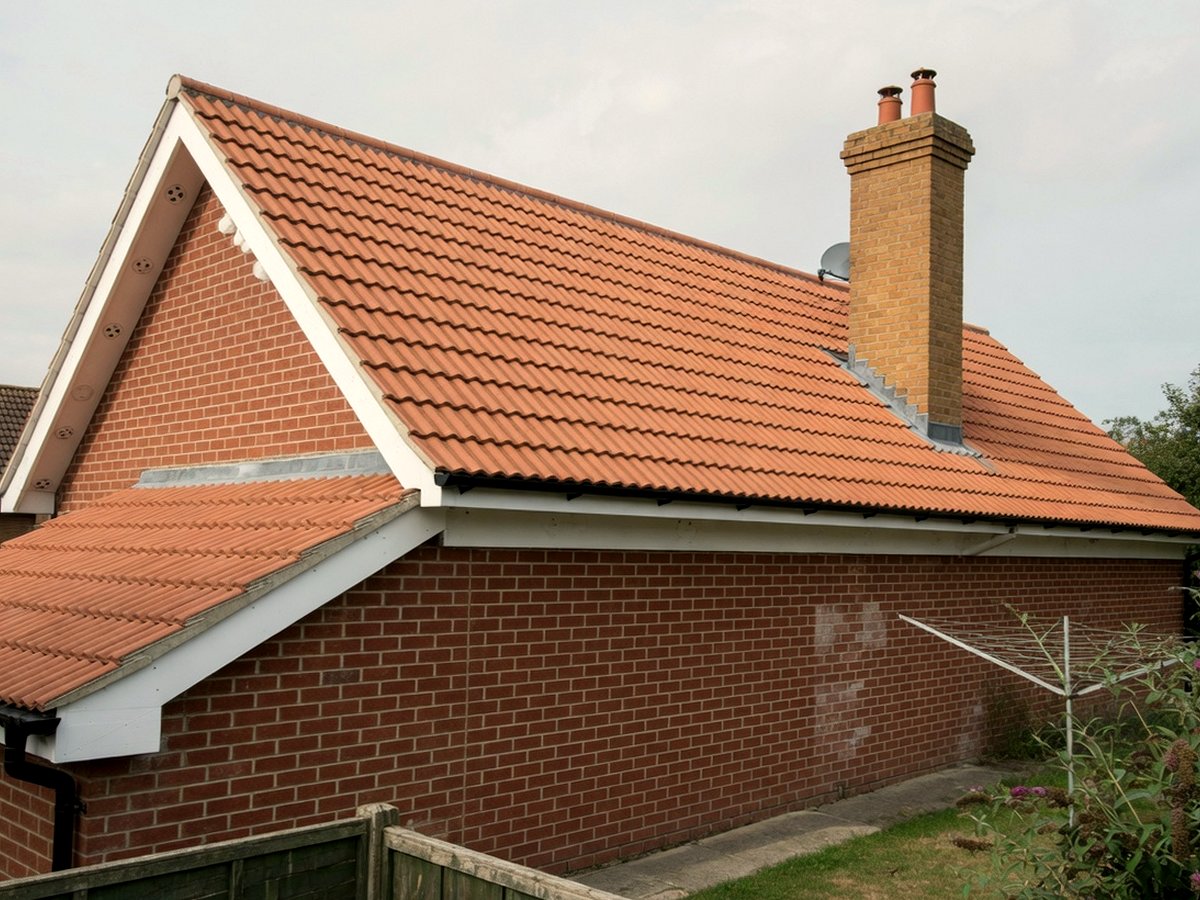 Completed clay-tiled pitched roof, white fascia and brick chimney on a UK house